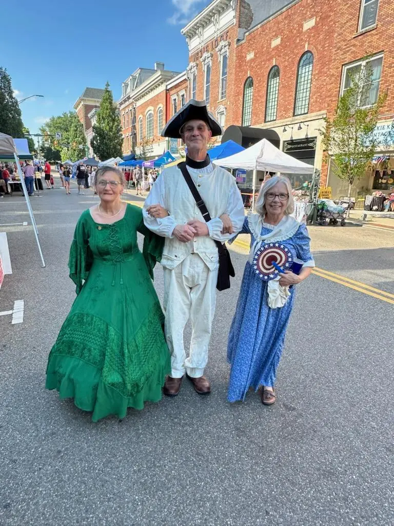 Two chapter members in colonial dress with a reenactor in a tricorn hat on Main Street
