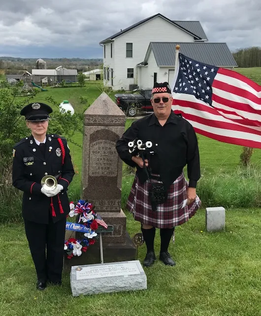 Bugler and bagpiper beside Jacob Dunham’s headstone, wreath, and new marker