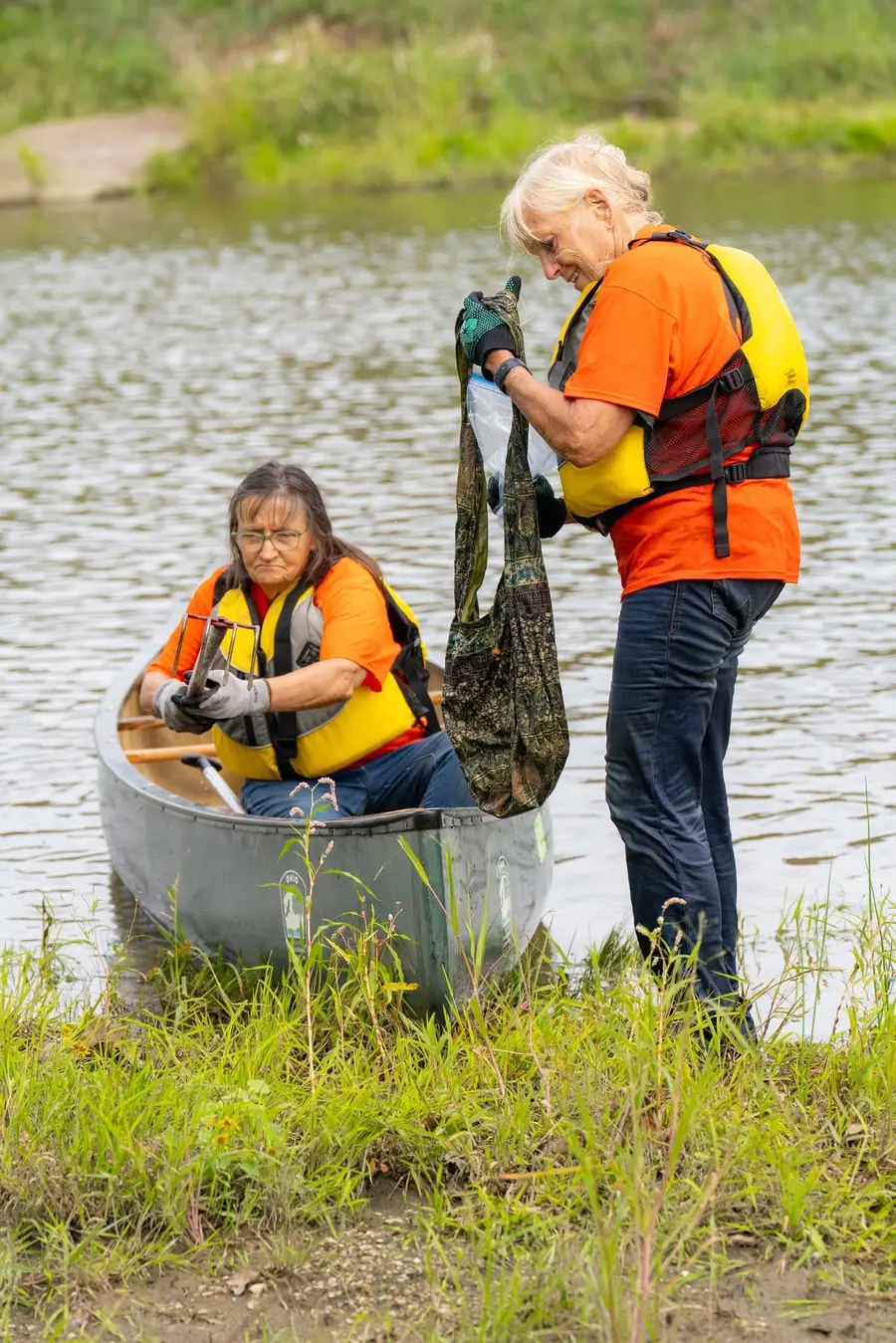 A member in a canoe passing a bag of trash to a volunteer on shore